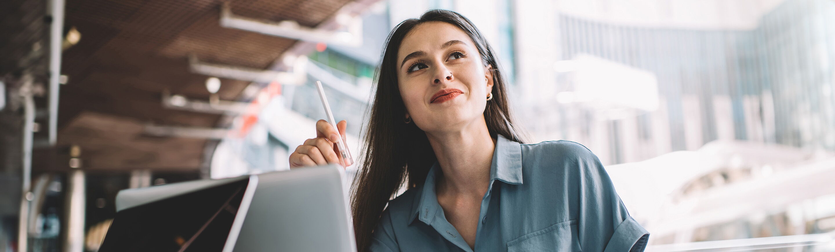 Eine nachdenkliche Frau sitzt an einem Laptop und plant ihre Karriere als Redakteurin in einem modernen Café.