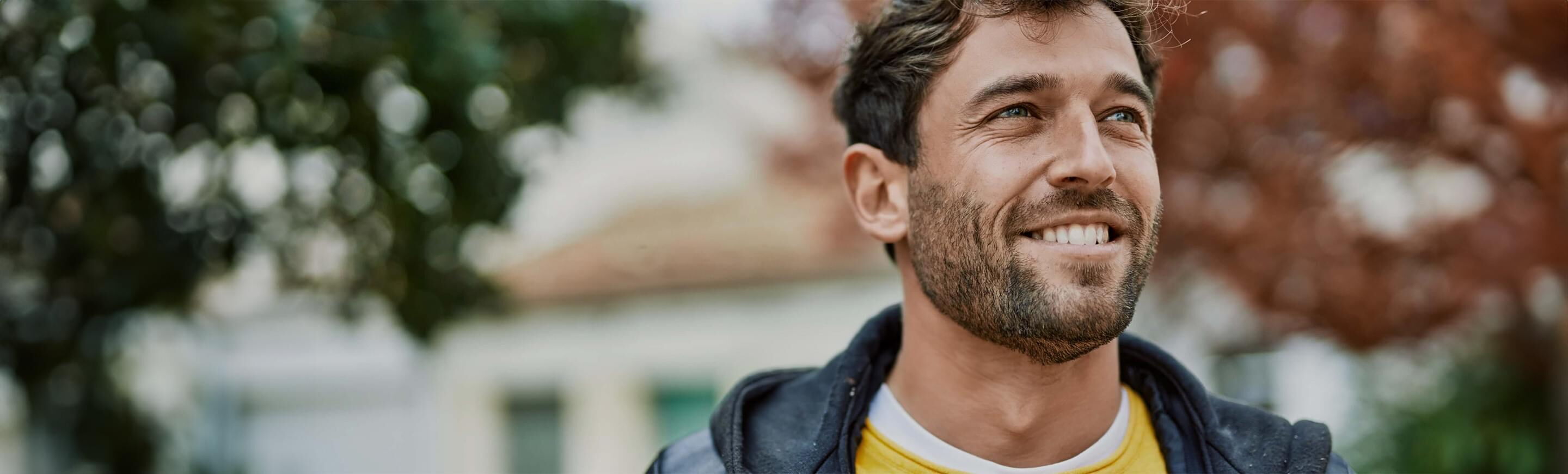 Ein junger Mann mit lächelndem Gesicht steht lässig im Freien und genießt die herbstliche Atmosphäre.