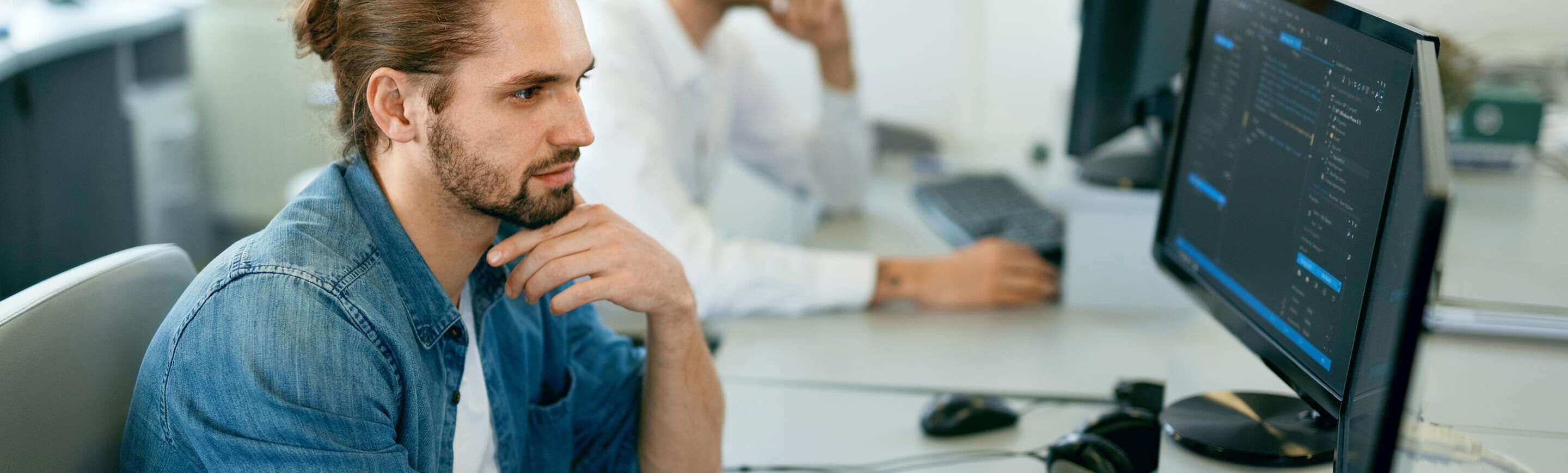 Ein junger Fachinformatiker konzentriert sich auf die Programmierung an einem Computerbildschirm in einem modernen Büro.