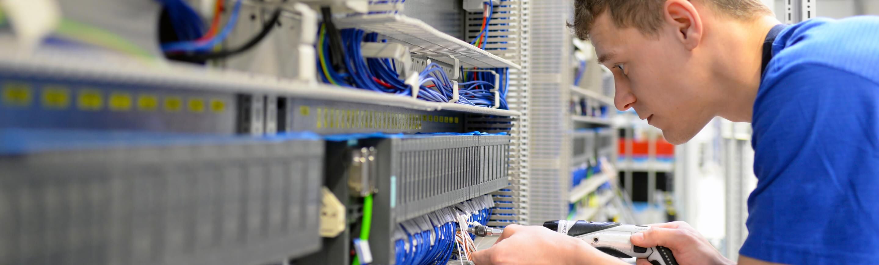 Ein Elektriker arbeitet konzentriert an einem Schaltschrank, während er Kabel anschließt und die Technik überprüft.