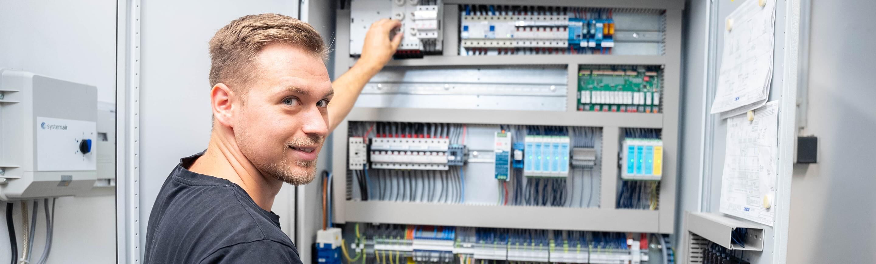 Ein Elektriker arbeitet konzentriert an einem Schaltschrank, während er Kabel anschließt und die Technik überprüft.